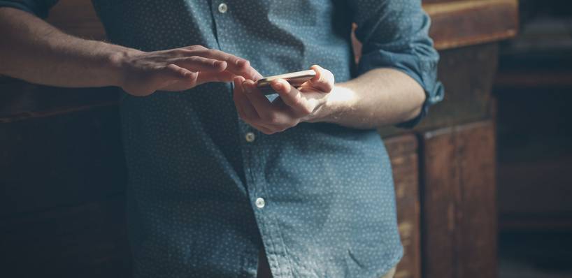 Hipster-Mann mit Smarphone lehnt an Möbel