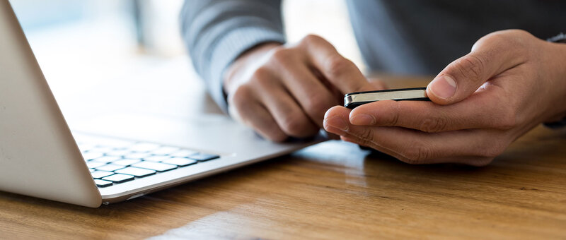 Mann mit Laptop und Smartphone in der Hand